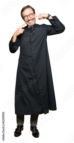 Middle age priest man wearing catholic robe smiling confident showing and pointing with fingers teeth and mouth. Health concept.