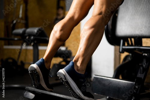 An unrecognizable bodybuilder is working the twins or gastrocnemius on a machine inside a gym. Concept of working legs, strong calves, lifting weight with gastrocnemius.