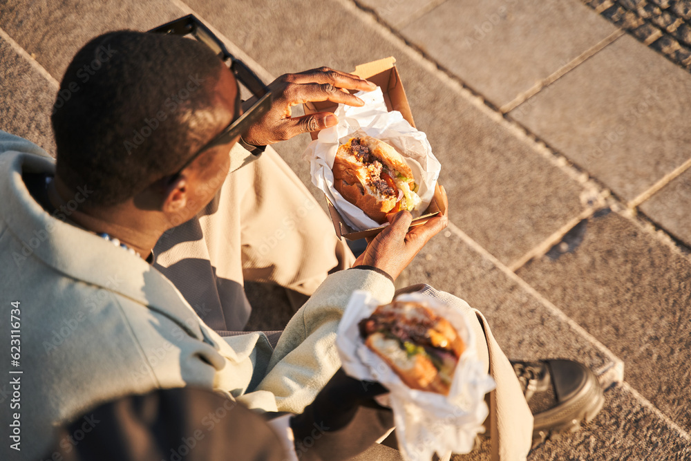 Obraz premium High angle view of the hipster guys eating fast food burgers while sitting on street stairs