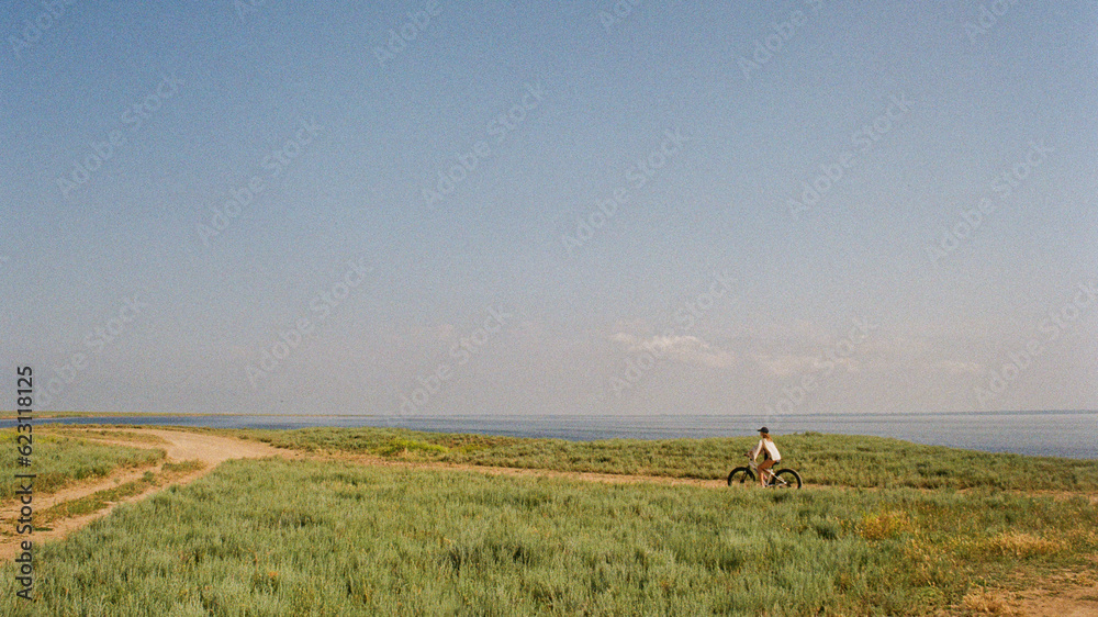 A person riding a bike in summer through a field next to a sea A person riding a bike in summer through a field next to a sea