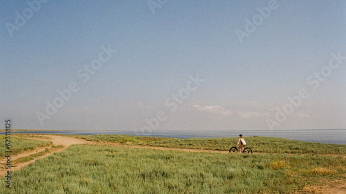 Fototapeta Naklejka Na Ścianę i Meble -  A person riding a bike in summer through a field next to a sea 