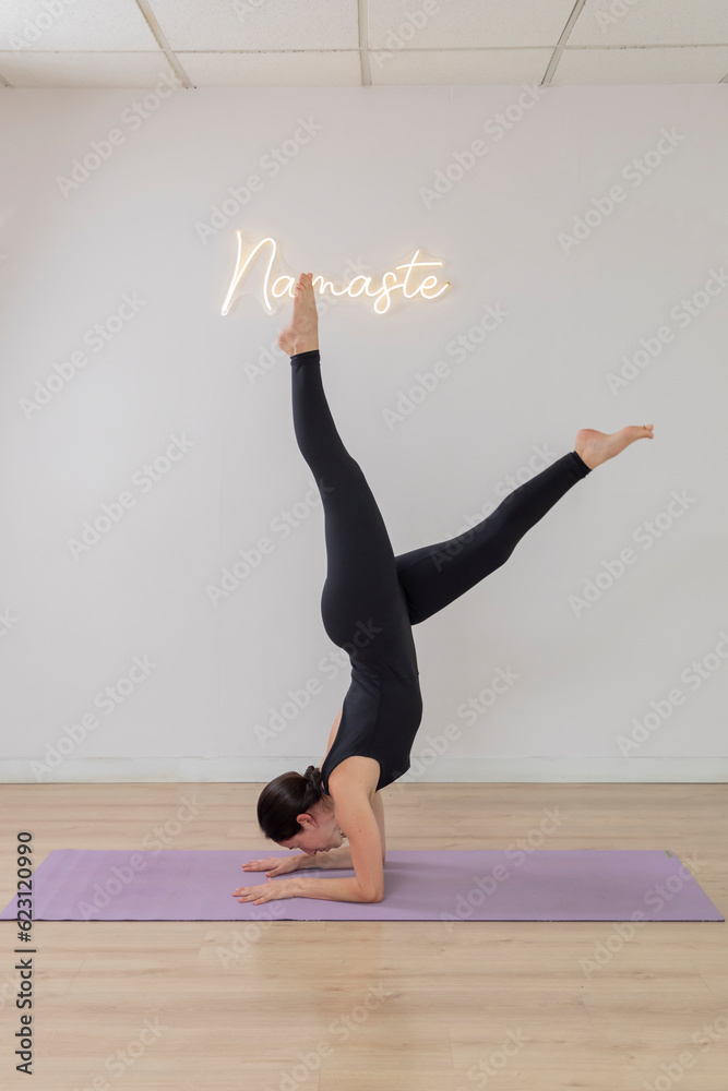 Young woman in sportswear practices yoga in a studio doing a handstand pose