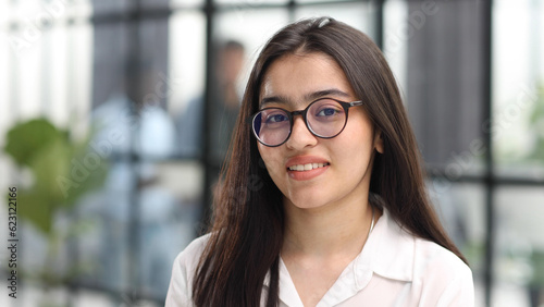 Close-up portrait of a confident and attractive woman in a white blouse and glasses in a classroom or office.