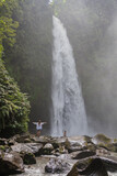 Young family mother with daughter travellers explore waterfall in Bali jungle, travel concept , vacation in Asia. 