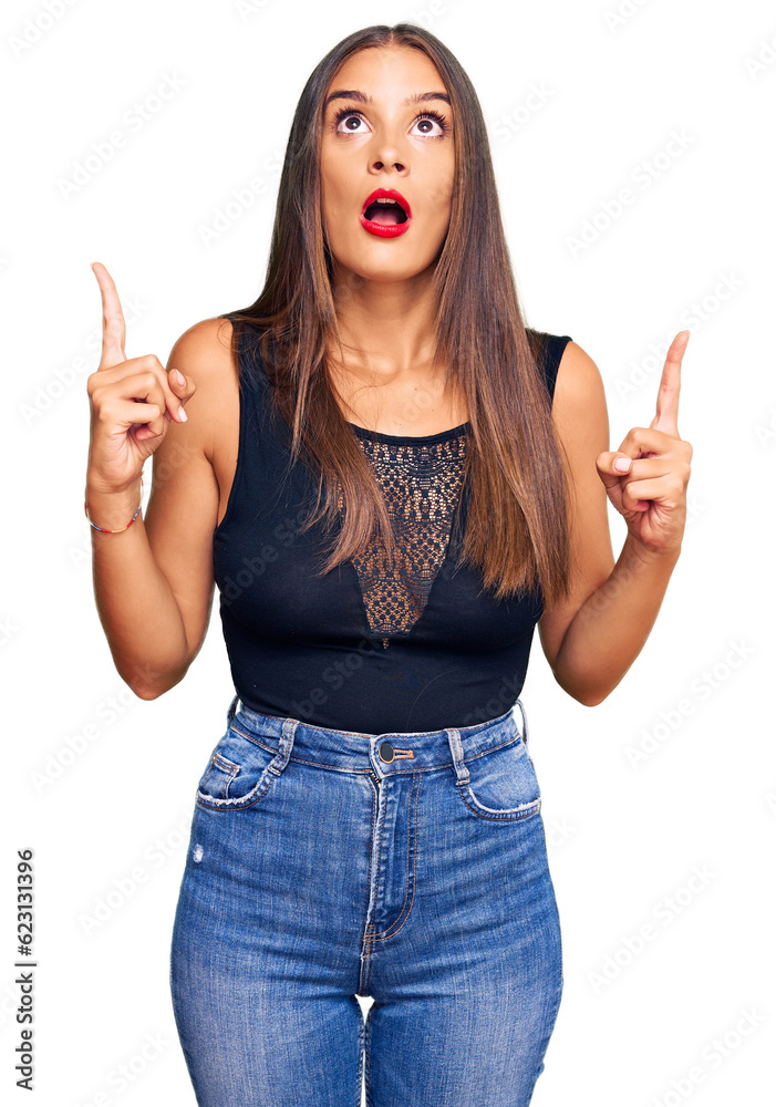 Young hispanic woman wearing casual clothes amazed and surprised looking up and pointing with fingers and raised arms. Young hispanic woman wearing casual clothes amazed and surprised looking up and pointing with fingers and raised arms.