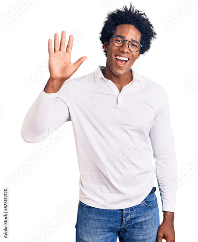 Handsome african american man with afro hair wearing casual clothes and glasses waiving saying hello happy and smiling, friendly welcome gesture