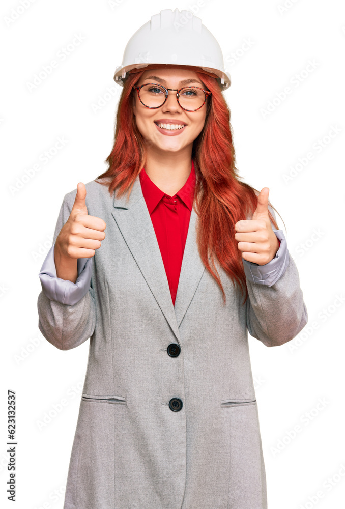 Young redhead woman wearing architect hardhat success sign doing positive gesture with hand, thumbs up smiling and happy. cheerful expression and winner gesture. Young redhead woman wearing architect hardhat success sign doing positive gesture with hand, thumbs up smiling and happy. cheerful expression and winner gesture.