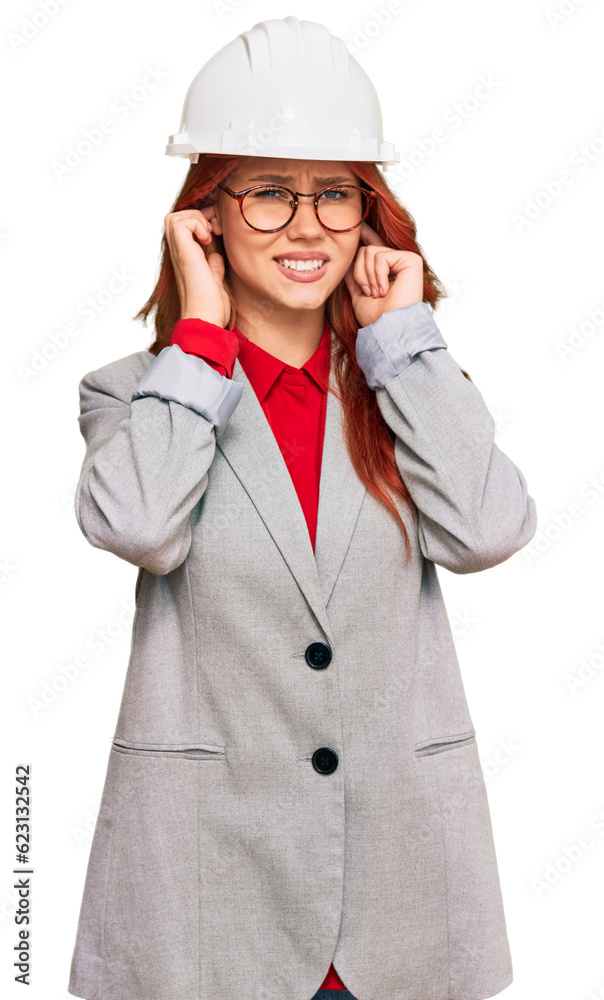 Young redhead woman wearing architect hardhat covering ears with fingers with annoyed expression for the noise of loud music. deaf concept. Young redhead woman wearing architect hardhat covering ears with fingers with annoyed expression for the noise of loud music. deaf concept.