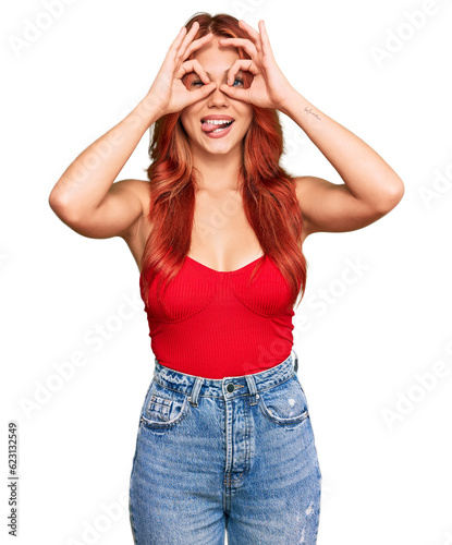 Young redhead woman wearing casual clothes doing ok gesture like binoculars sticking tongue out, eyes looking through fingers. crazy expression.