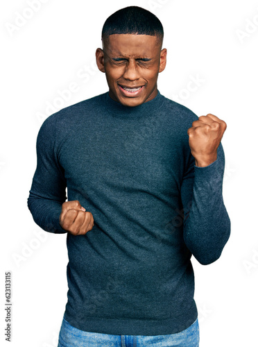 Young black man wearing casual sweater celebrating surprised and amazed for success with arms raised and eyes closed