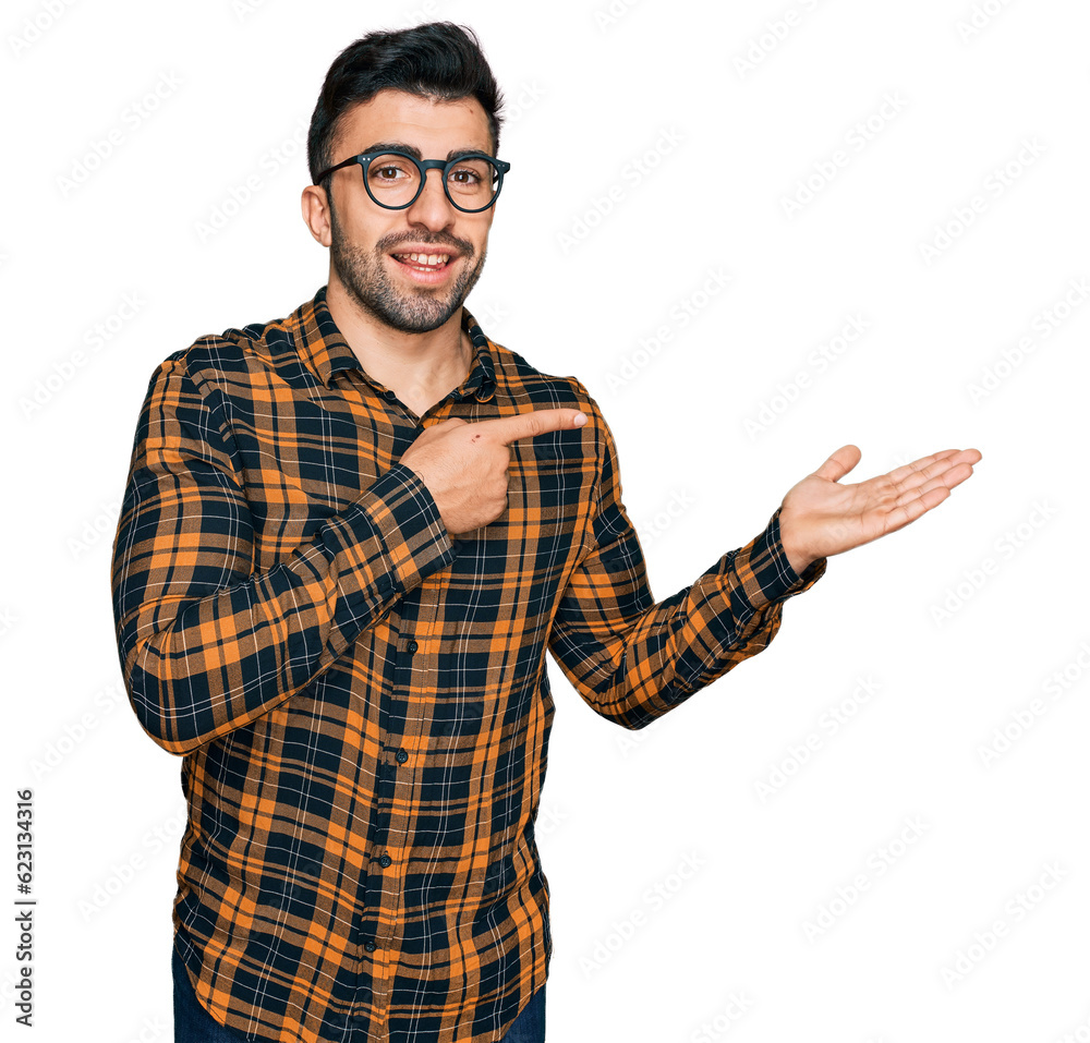Hispanic man with beard wearing casual clothes and glasses amazed and smiling to the camera while presenting with hand and pointing with finger. Hispanic man with beard wearing casual clothes and glasses amazed and smiling to the camera while presenting with hand and pointing with finger.