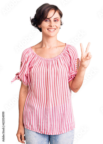 Beautiful young woman with short hair wearing casual summer clothes smiling looking to the camera showing fingers doing victory sign. number two.
