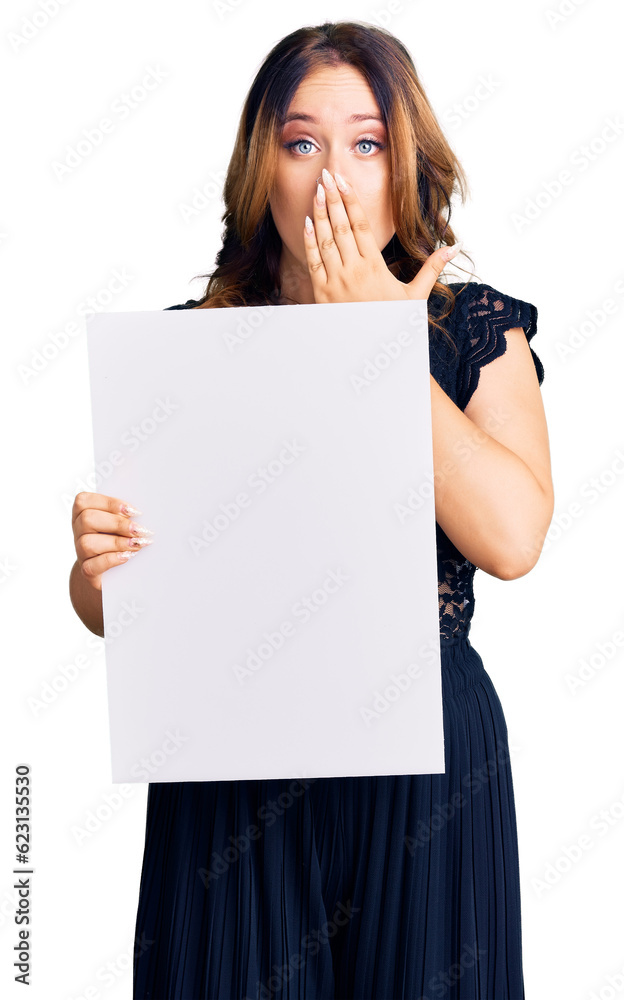 Young beautiful caucasian woman holding cardboard banner with blank space covering mouth with hand, shocked and afraid for mistake. surprised expression Young beautiful caucasian woman holding cardboard banner with blank space covering mouth with hand, shocked and afraid for mistake. surprised expression
