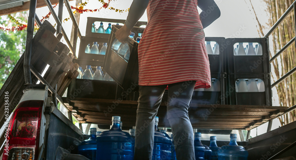 Workers lift blue drinking water bottles in crates into the back of a ...