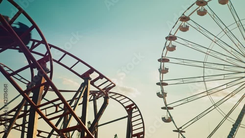 Entertainment for children during school holidays. Twisting red roller coaster and Ferris wheel Silhouettes at sunset. Funfair and amusement park