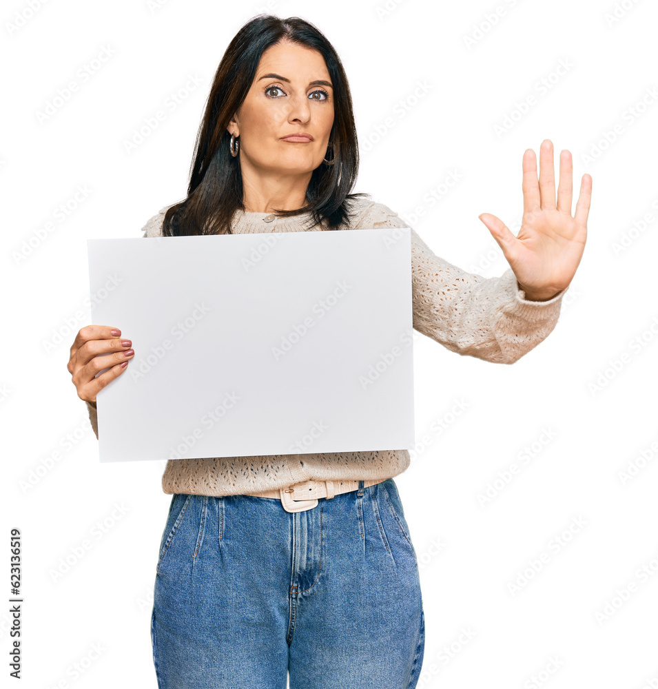 Middle age brunette woman holding blank empty banner with open hand doing stop sign with serious and confident expression, defense gesture Middle age brunette woman holding blank empty banner with open hand doing stop sign with serious and confident expression, defense gesture