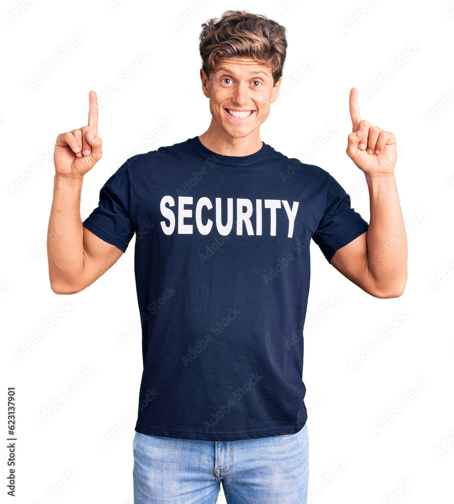 Young handsome man wearing security t shirt smiling amazed and surprised and pointing up with fingers and raised arms. Young handsome man wearing security t shirt smiling amazed and surprised and pointing up with fingers and raised arms.