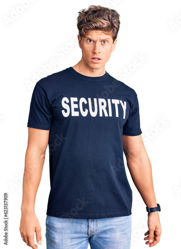Young handsome man wearing security t shirt in shock face, looking skeptical and sarcastic, surprised with open mouth