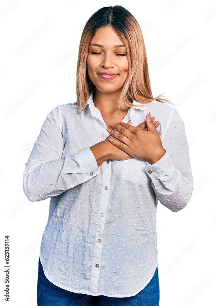 Young hispanic woman wearing casual white shirt smiling with hands on chest with closed eyes and grateful gesture on face. health concept. Young hispanic woman wearing casual white shirt smiling with hands on chest with closed eyes and grateful gesture on face. health concept.