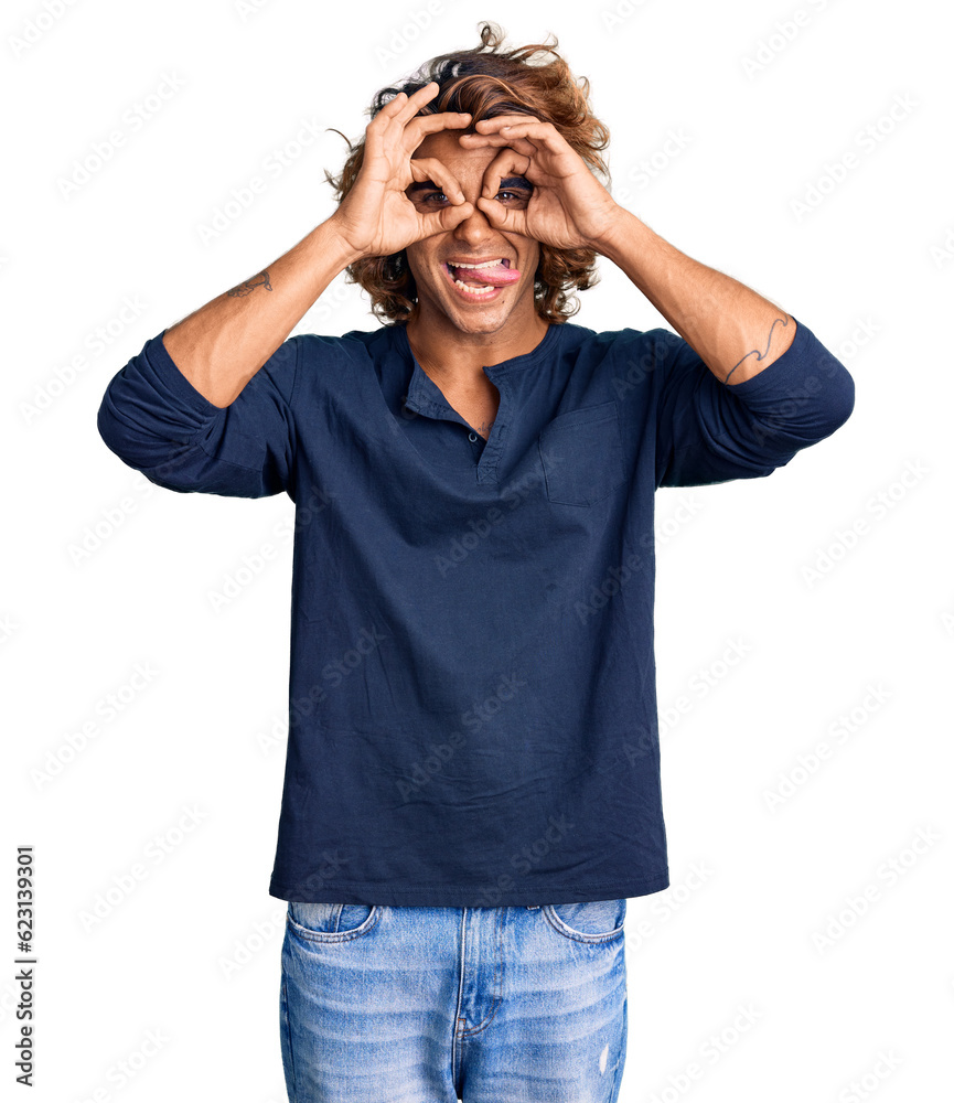 Young hispanic man wearing casual clothes doing ok gesture like binoculars sticking tongue out, eyes looking through fingers. crazy expression. Young hispanic man wearing casual clothes doing ok gesture like binoculars sticking tongue out, eyes looking through fingers. crazy expression.