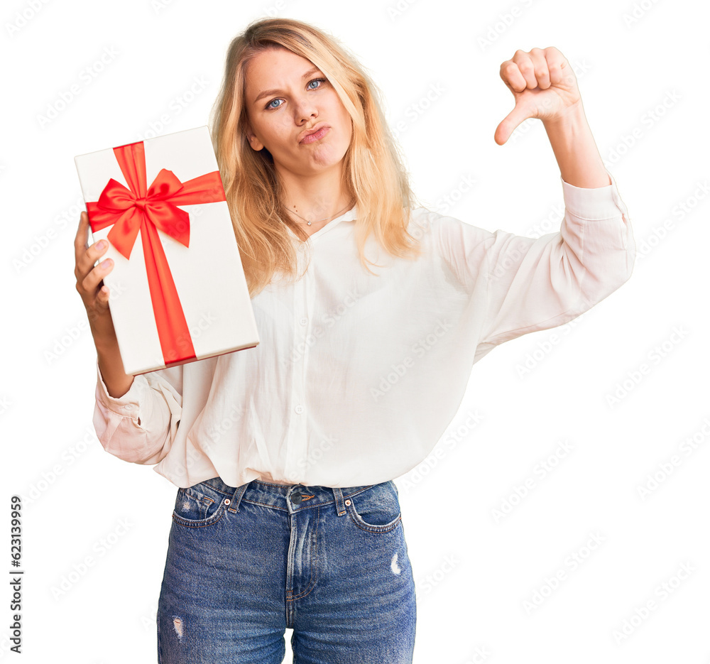 Young beautiful blonde woman holding gift smiling happy pointing with hand and finger Young beautiful blonde woman holding gift smiling happy pointing with hand and finger