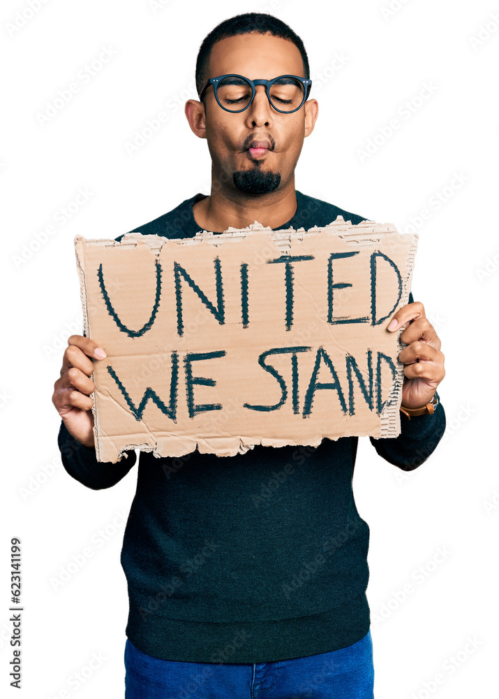 Young african american man holding united we stand banner making fish face with mouth and squinting eyes, crazy and comical. Young african american man holding united we stand banner making fish face with mouth and squinting eyes, crazy and comical.