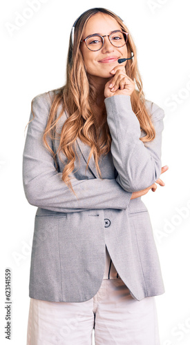 Young beautiful blonde woman wearing call center agent headset looking confident at the camera with smile with crossed arms and hand raised on chin. thinking positive. photo