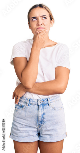 Young beautiful blonde woman wearing casual white tshirt with hand on chin thinking about question, pensive expression. smiling with thoughtful face. doubt concept. photo