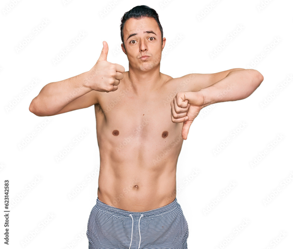 Handsome young man wearing swimwear shirtless doing thumbs up and down, disagreement and agreement expression. crazy conflict Handsome young man wearing swimwear shirtless doing thumbs up and down, disagreement and agreement expression. crazy conflict