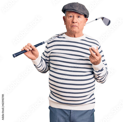 Senior handsome grey-haired man holding golf club and ball thinking attitude and sober expression looking self confident