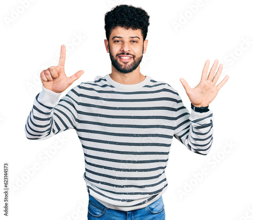 Young arab man with beard wearing casual striped sweater showing and pointing up with fingers number seven while smiling confident and happy.