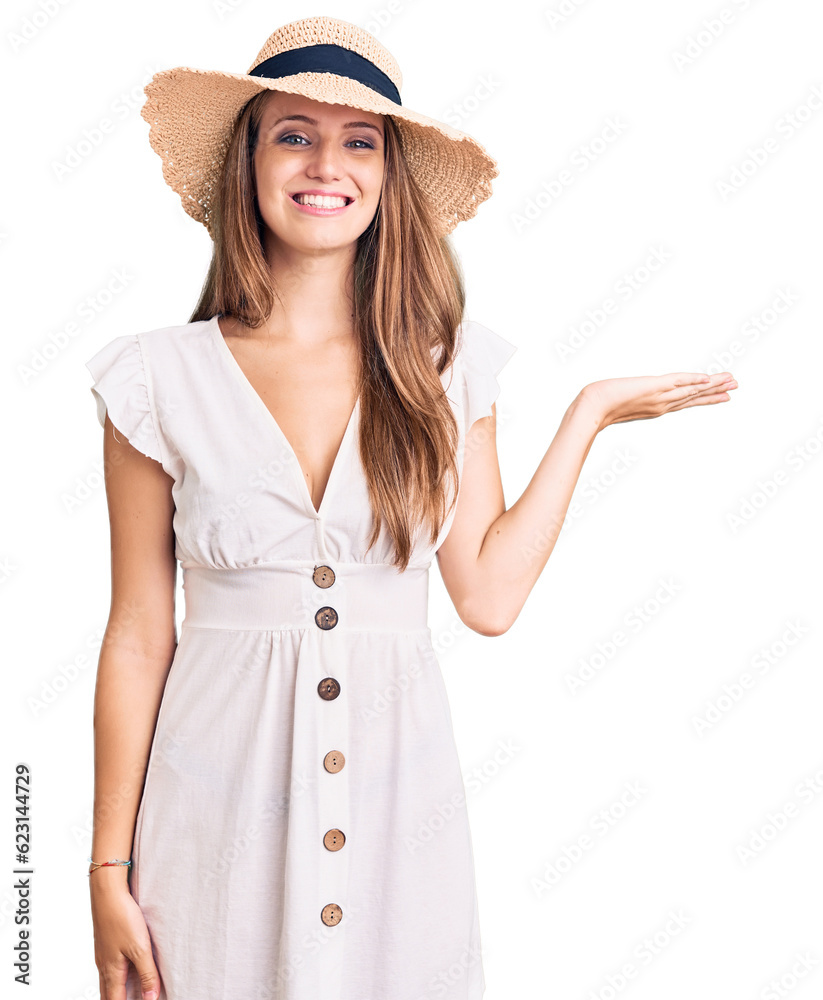 Young beautiful blonde woman wearing summer dress and hat smiling cheerful presenting and pointing with palm of hand looking at the camera. Young beautiful blonde woman wearing summer dress and hat smiling cheerful presenting and pointing with palm of hand looking at the camera.
