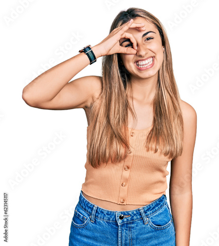 Hispanic young woman wearing casual summer shirt doing ok gesture with hand smiling, eye looking through fingers with happy face.