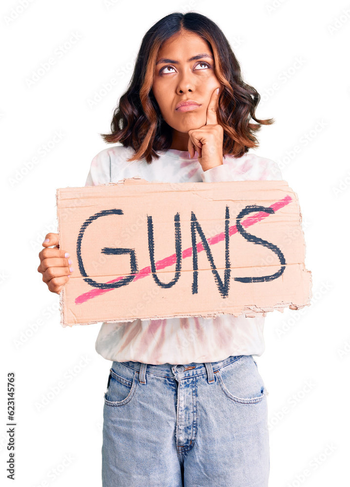 Young beautiful mixed race woman holding no guns warning banner serious face thinking about question with hand on chin, thoughtful about confusing idea
