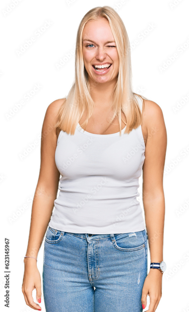 Fototapeta premium Young blonde girl wearing casual style with sleeveless shirt winking looking at the camera with sexy expression, cheerful and happy face.
