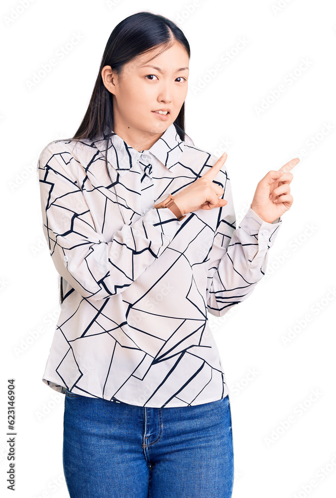 Young beautiful chinese woman wearing casual shirt pointing aside worried and nervous with both hands, concerned and surprised expression Young beautiful chinese woman wearing casual shirt pointing aside worried and nervous with both hands, concerned and surprised expression