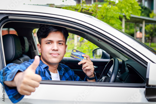 Young Asian man sitting in a car holding a credit card and smiling happily. Cash card concept, car insurance. transportation