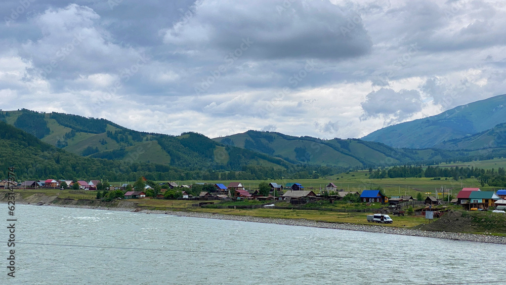 Russian village on the bank of the Katun River, Altai, Russia. Green wooded hills, ridges and mountains. View from the height of the Katun River.