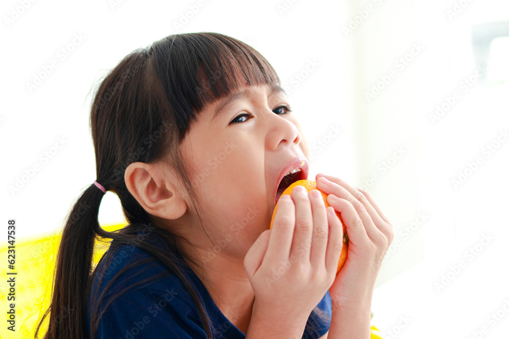 An Asian little girl is eating a very sour orange. food nutrition concept for kids An Asian little girl is eating a very sour orange. food nutrition concept for kids