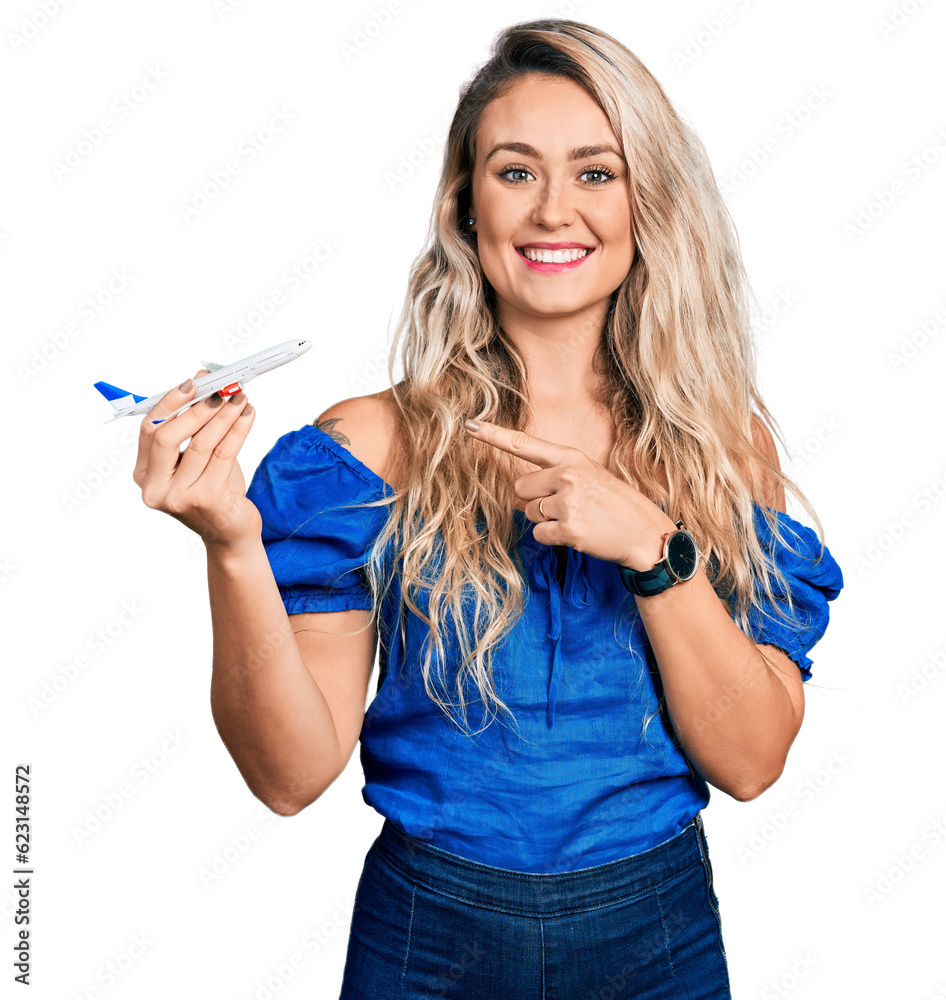 Young blonde woman holding airplane toy smiling happy pointing with hand and finger Young blonde woman holding airplane toy smiling happy pointing with hand and finger