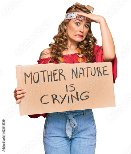 Young blonde girl wearing hippie style holding mother nature is crying protest cardboard banner stressed and frustrated with hand on head, surprised and angry face