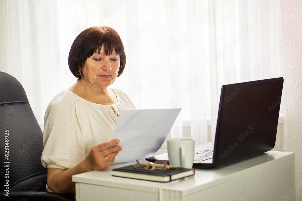 Middle aged senior woman sitting with laptop and paper document, working and drinking coffee. Middle aged senior woman sitting with laptop and paper document, working and drinking coffee.