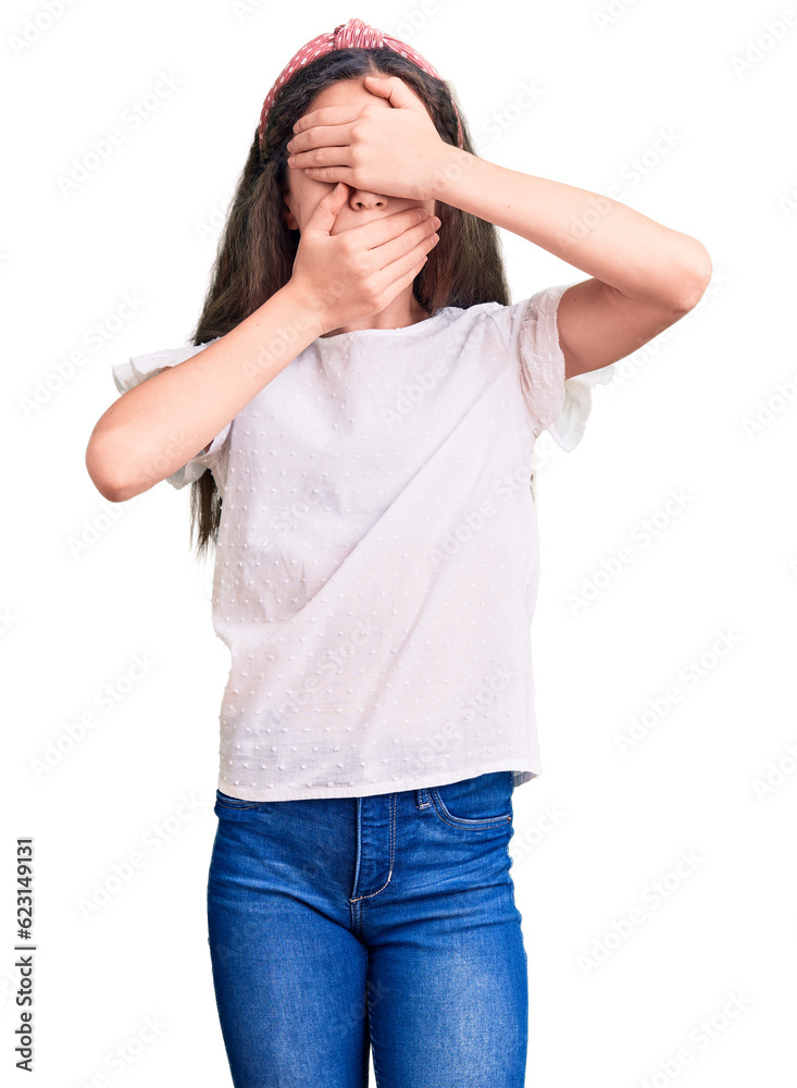 Cute hispanic child girl wearing casual white tshirt covering eyes and mouth with hands, surprised and shocked. hiding emotion Cute hispanic child girl wearing casual white tshirt covering eyes and mouth with hands, surprised and shocked. hiding emotion