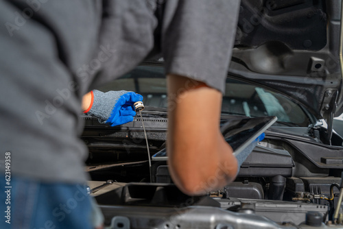 A male car mechanic checking car motor oil and working on repairing the car at car repair garage