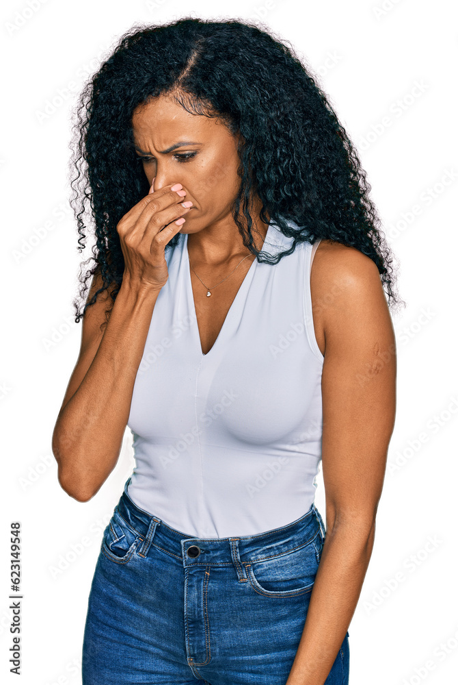 Middle age african american woman wearing casual style with sleeveless shirt smelling something stinky and disgusting, intolerable smell, holding breath with fingers on nose. bad smell Middle age african american woman wearing casual style with sleeveless shirt smelling something stinky and disgusting, intolerable smell, holding breath with fingers on nose. bad smell
