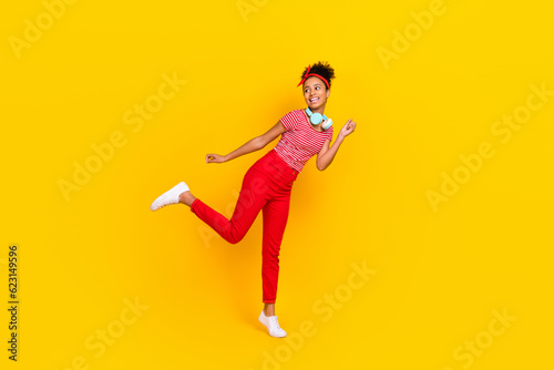 Full size photo of funky young girl dance enjoy music favorite song wear trendy red striped clothes isolated on yellow color background