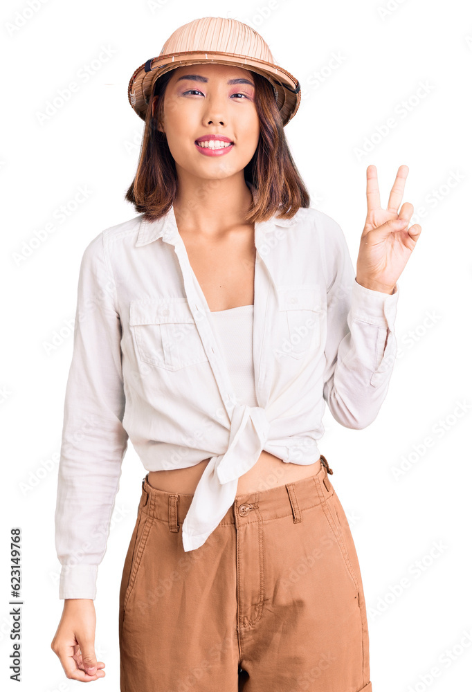 Young beautiful chinese girl wearing explorer hat smiling with happy face winking at the camera doing victory sign. number two. Young beautiful chinese girl wearing explorer hat smiling with happy face winking at the camera doing victory sign. number two.