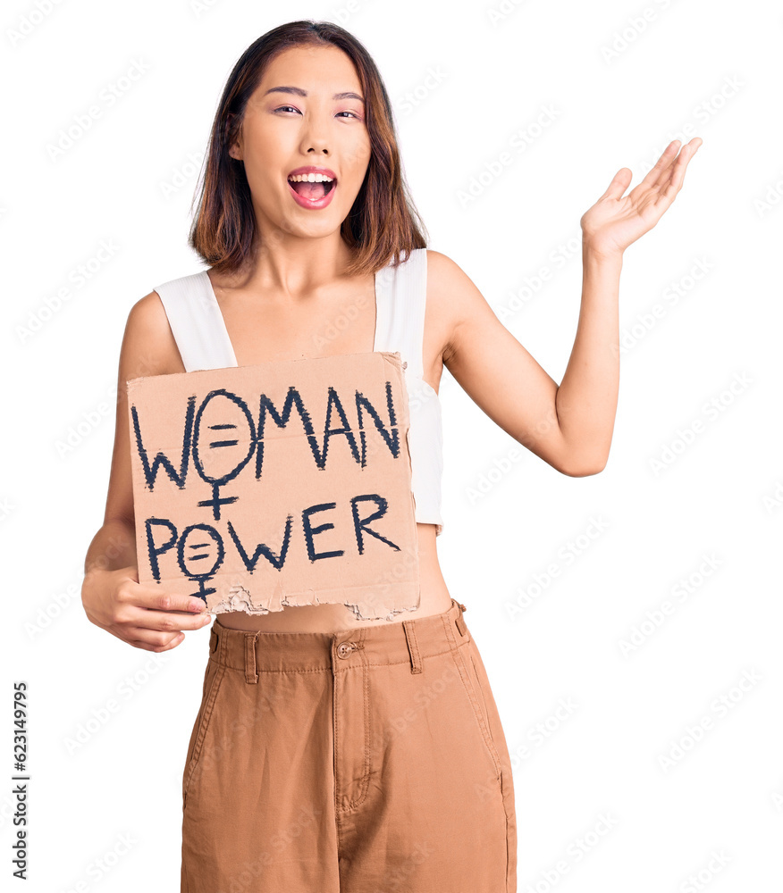 Young beautiful chinese girl holding woman power banner celebrating victory with happy smile and winner expression with raised hands Young beautiful chinese girl holding woman power banner celebrating victory with happy smile and winner expression with raised hands