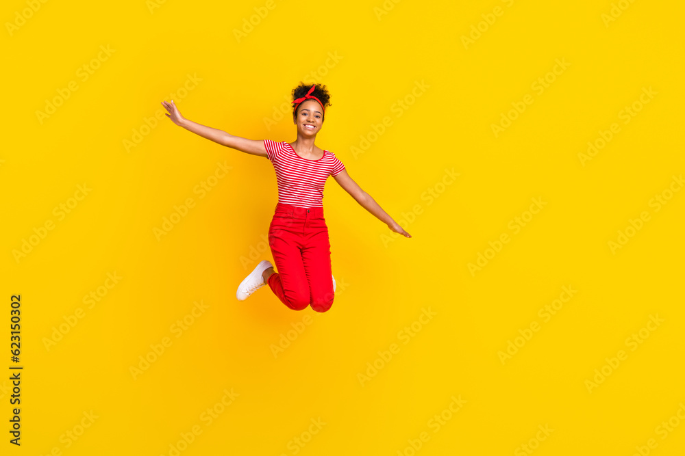 Full size photo of funky young girl jumping spread hands flight dressed stylish red striped clothes isolated on yellow color background