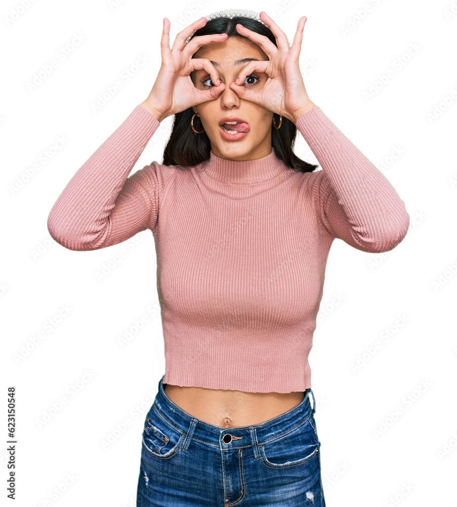 Young hispanic girl wearing casual clothes doing ok gesture like binoculars sticking tongue out, eyes looking through fingers. crazy expression. Young hispanic girl wearing casual clothes doing ok gesture like binoculars sticking tongue out, eyes looking through fingers. crazy expression.
